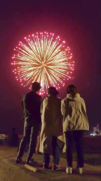 還暦を象徴する【赤い】花火を還暦を迎える方とそのご家族で見上げている画像になります。